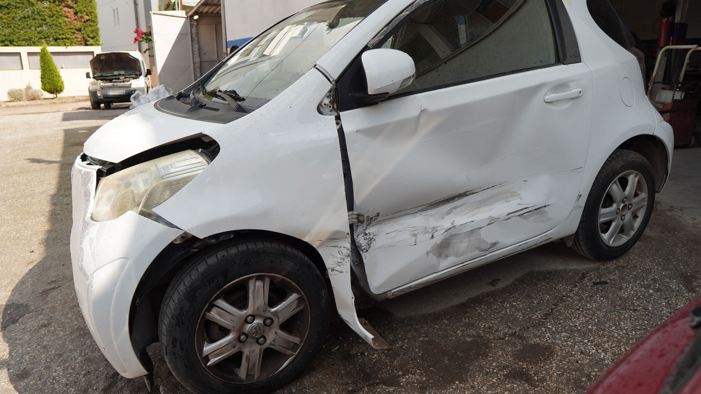 Πριν — λευκό Toyota iQ με χτυπημένο εμπρός φτερό, πόρτα και μαρσπιέ στην πλευρά του οδηγού